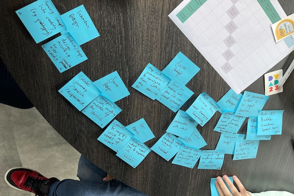 A circular table with post-it notes with writing on them, stickers, a Sharpie and print out of a grid on it. 