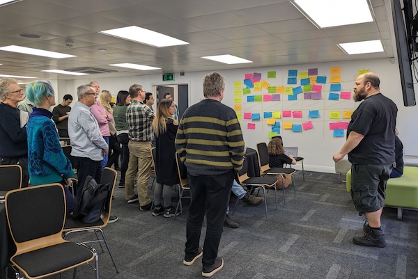 UK Charity Camp attendees standing in front of a wall full of post-its with suggested discussion topics on them.