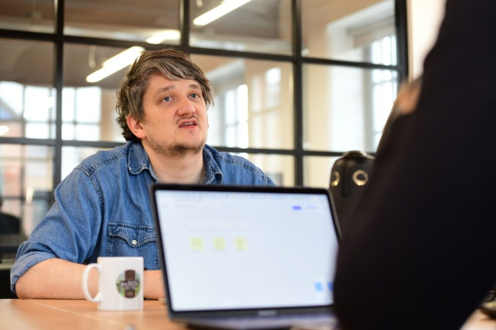 A person in a meeting talking to someone using a laptop