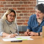 2 people in a meeting writing on post its